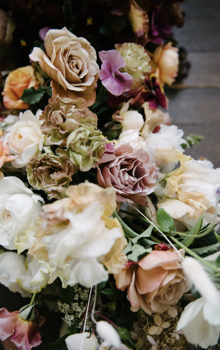 A bouquet of various pastel-colored flowers including roses, carnations, and sweet peas, arranged on a wooden surface.
