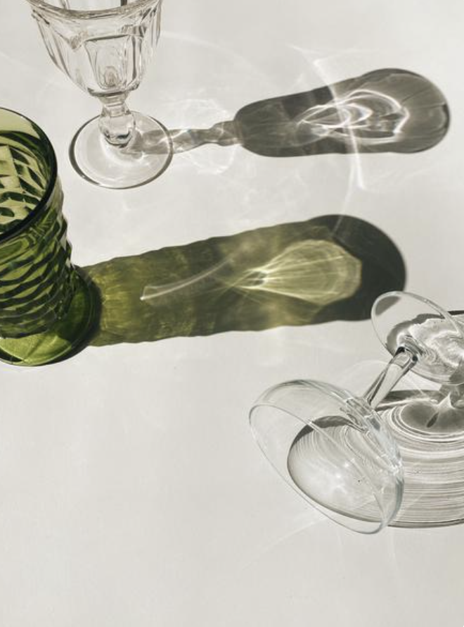 Two upside-down wine glasses and a green glass vase casting colorful shadows on a white surface.