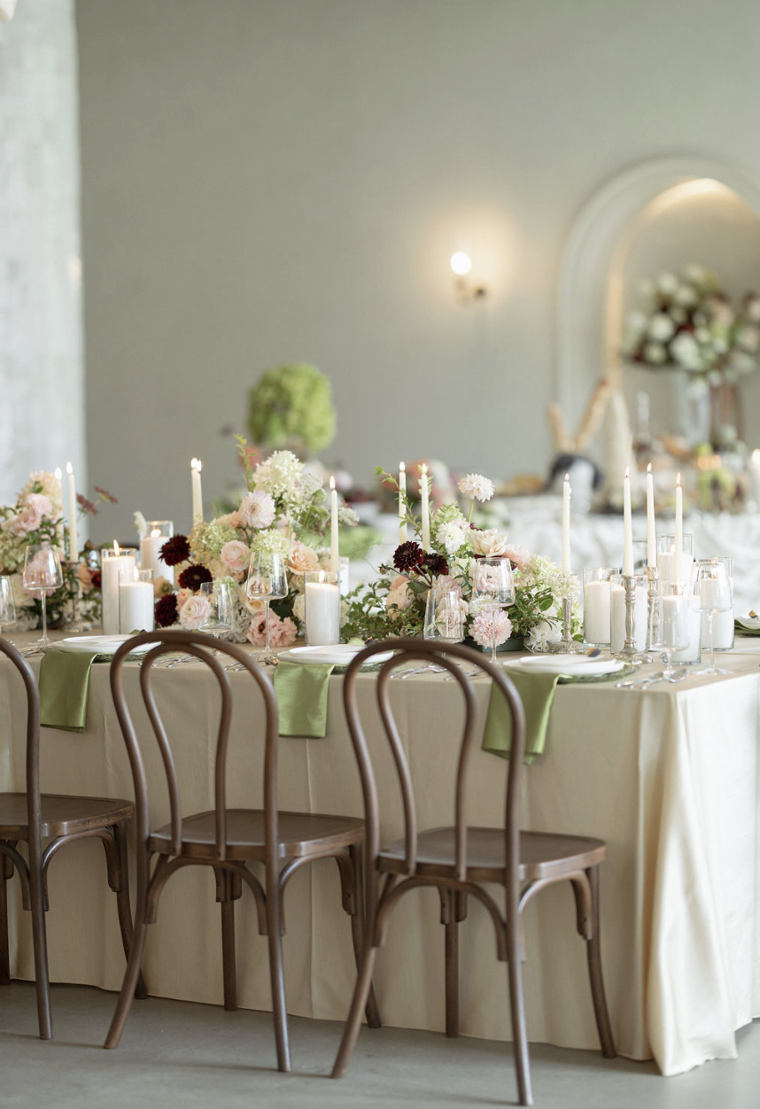 Elegant dining table decorated with floral centerpieces, candles, and glasses at a formal event or wedding reception.