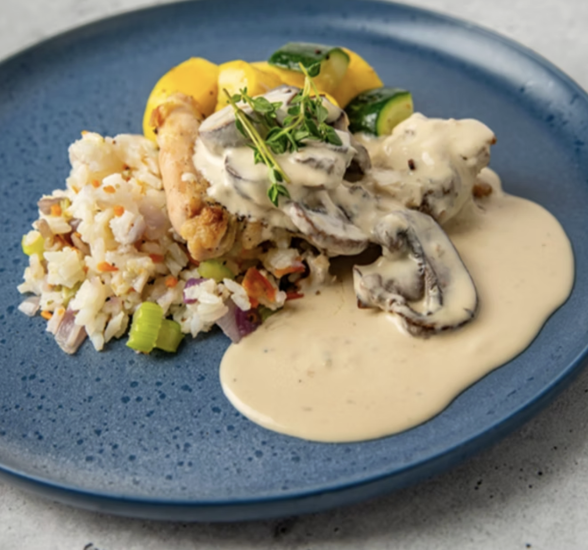 Plate of chicken with mushroom cream sauce, topped with fresh herbs, served with rice pilaf and zucchini with yellow squash.