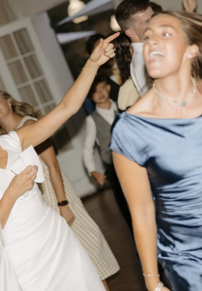 People dancing at a party, with a woman's hand pointing in the air and people smiling in the background.