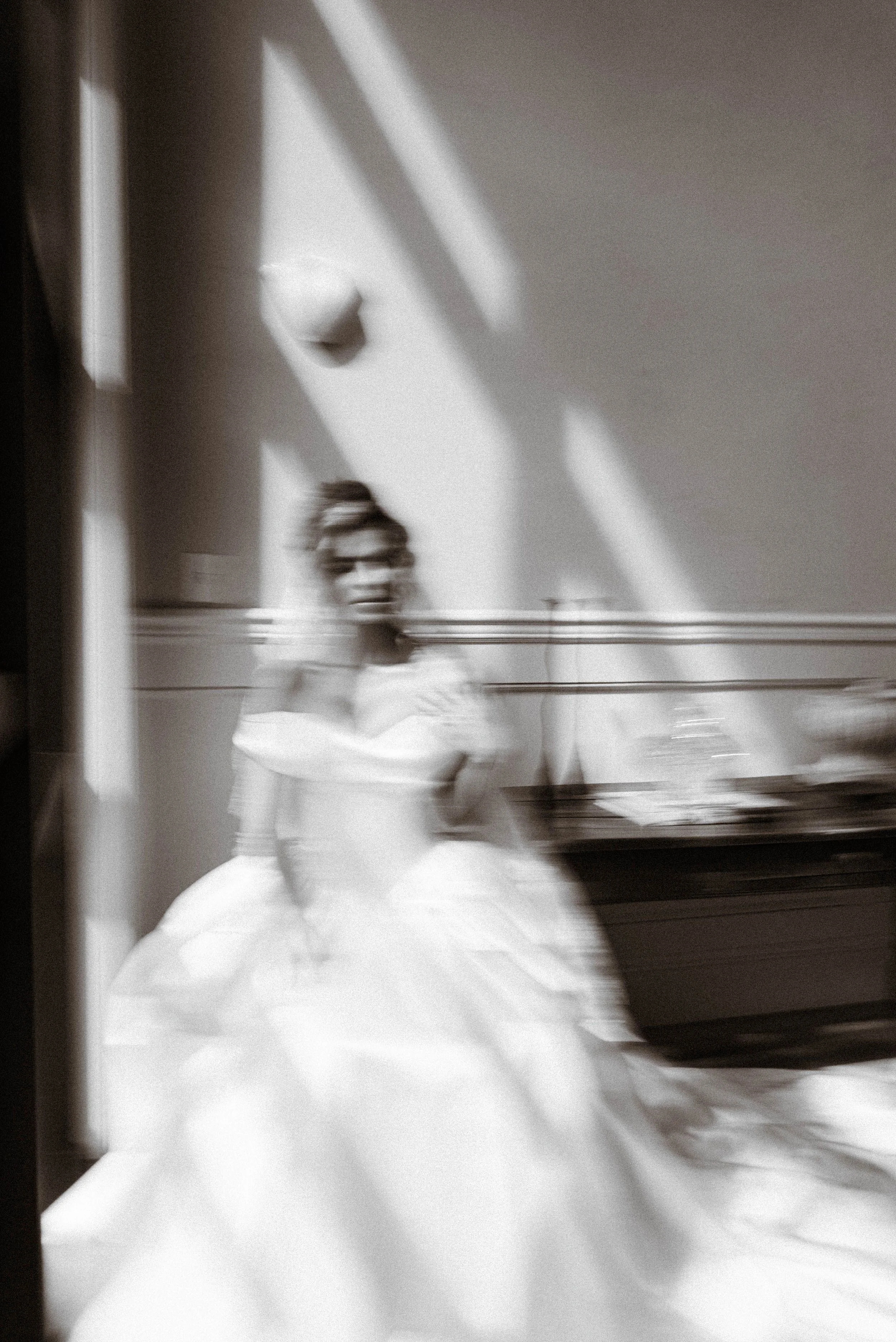 A person in a white dress walking in a room with sunlight and shadows on the wall.
