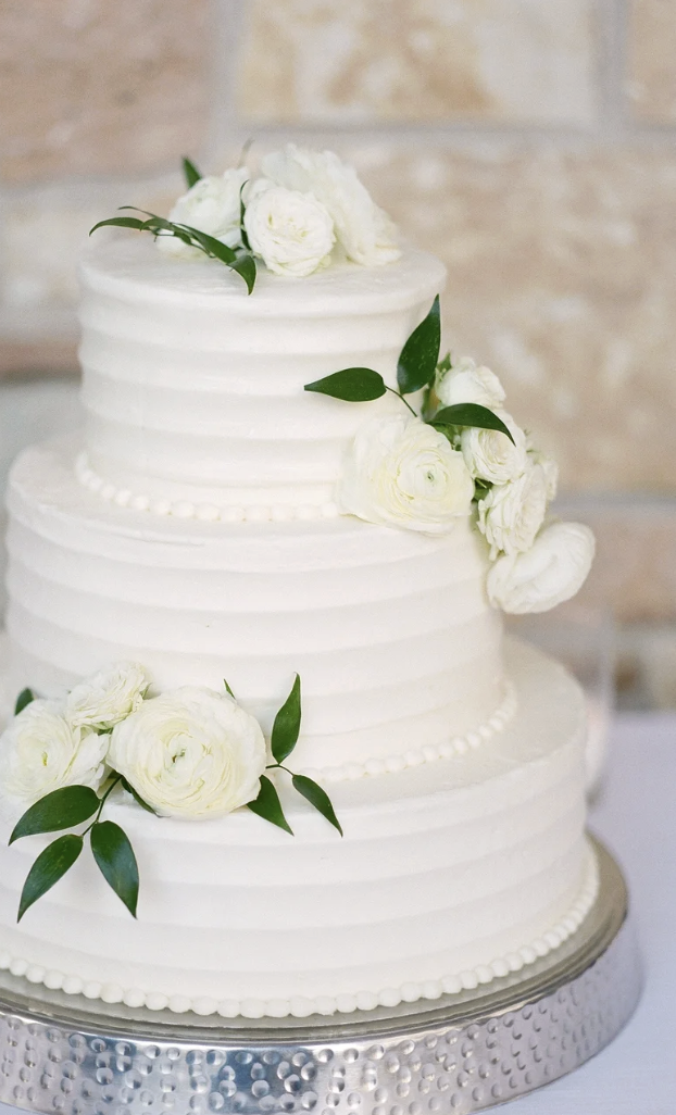 A three-tier white wedding cake decorated with white roses and green leaves.