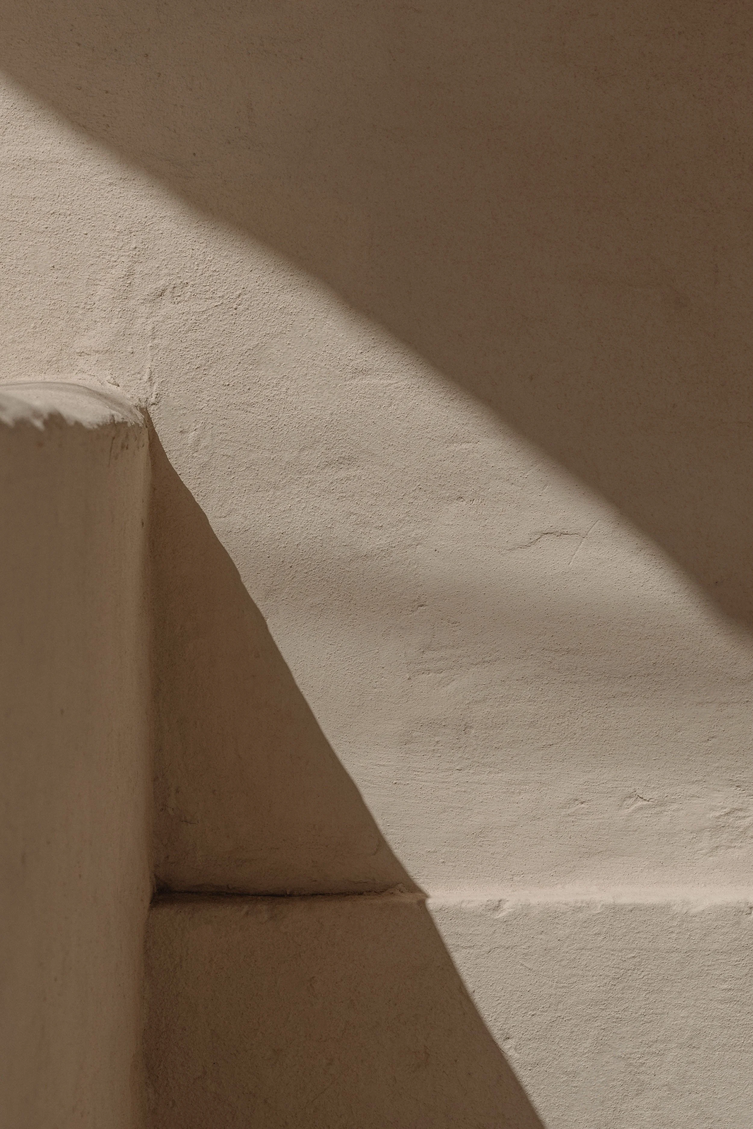 Close-up of a corner of a ceiling and wall with textured beige paint, and a diagonal shadow cast across the surface.