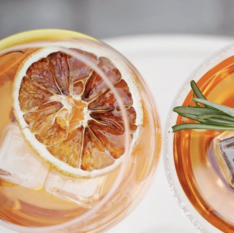 Close-up of two glasses of iced tea with lemon slices, ice cubes, and a sprig of rosemary on a white surface.