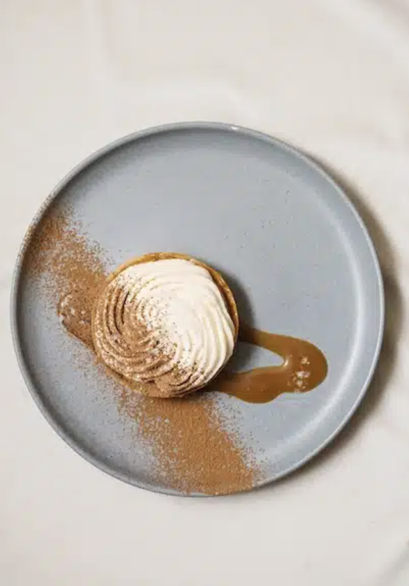 A dessert with whipped cream, caramel sauce, and cocoa powder on a light gray plate.