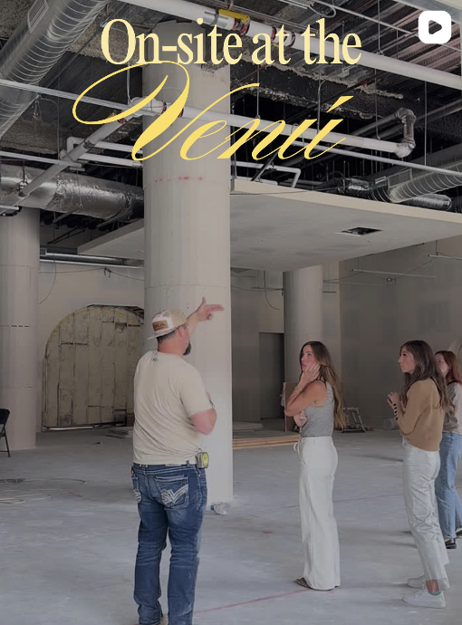 A construction site tour with a guide explaining to three women in an unfinished building with exposed pipes and concrete pillars.
