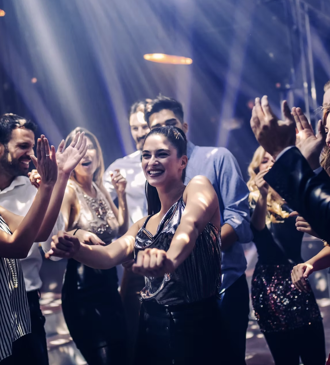 Group of people dancing and celebrating at a party or club with colorful lighting.