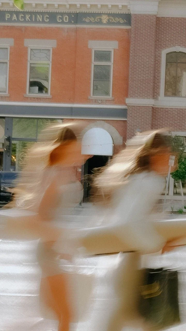 Two women walking past a brick building with a sign reading 'Packing Co', captured with motion blur.