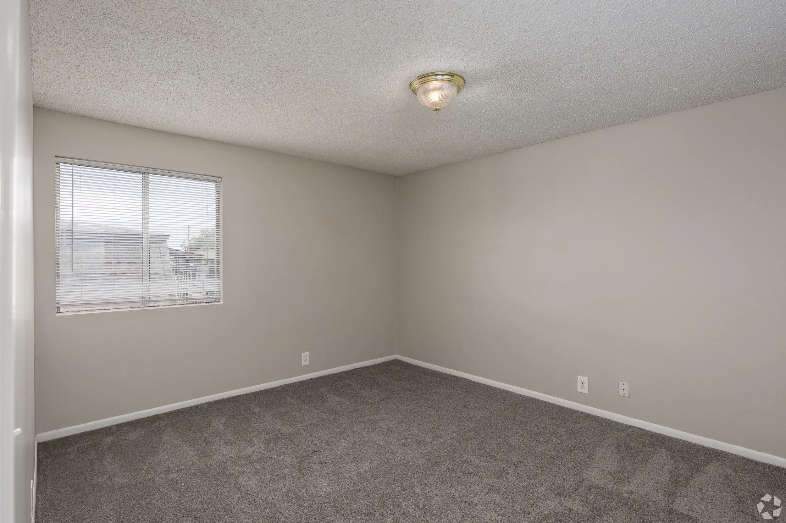 Empty room with beige walls, window with blinds, a ceiling light fixture, and carpeted floor.