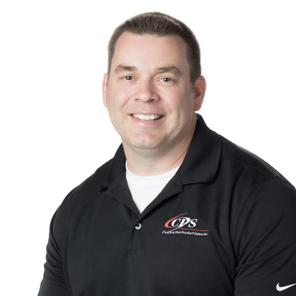 A man smiling, wearing a black polo shirt with a logo on it, against a plain white background.