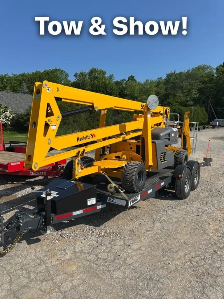 A yellow tow truck attachment mounted on a black trailer labeled 'PRATT EZ 2500' parked on a dirt lot, with a blue sky and green trees in the background. The image has the text 'Tow & Show!' at the top.