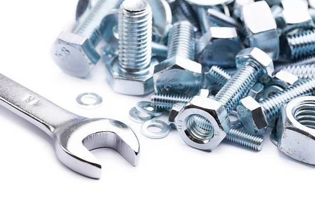 Metal nuts, bolts, washers, and an open wrench on a white surface.