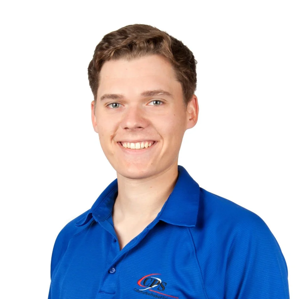A young man with short brown hair smiling and wearing a blue button-up shirt with a logo, against a white background.