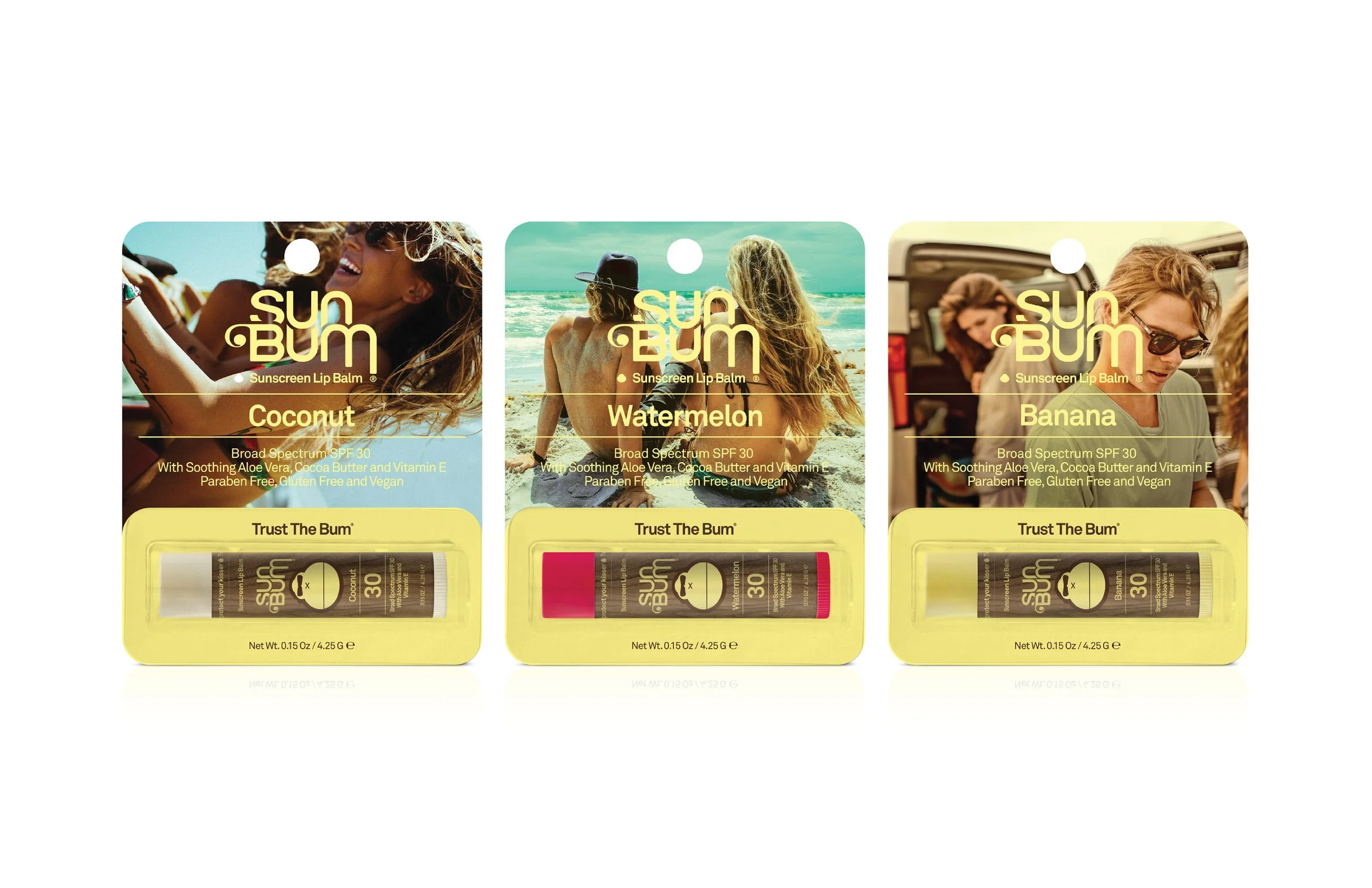 Three Tropicsun Bum sunscreen lip balms with coconut, watermelon, and banana flavors, each in yellow packaging, displayed in front of images of people on the beach and outdoors.