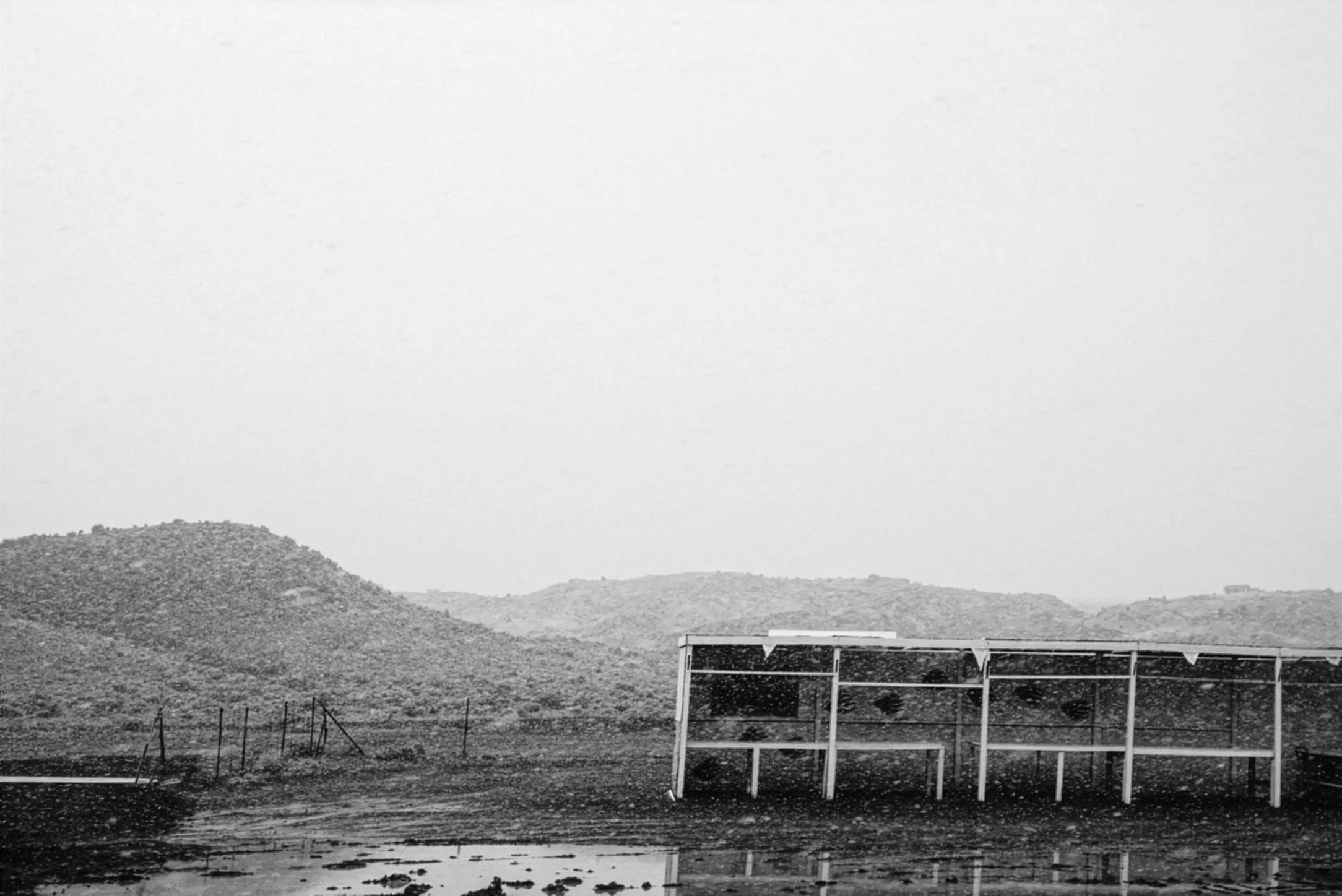 Black and white photo of a landscape with mountains in the background, a body of water in the foreground, and solar panels on a structure near the water.