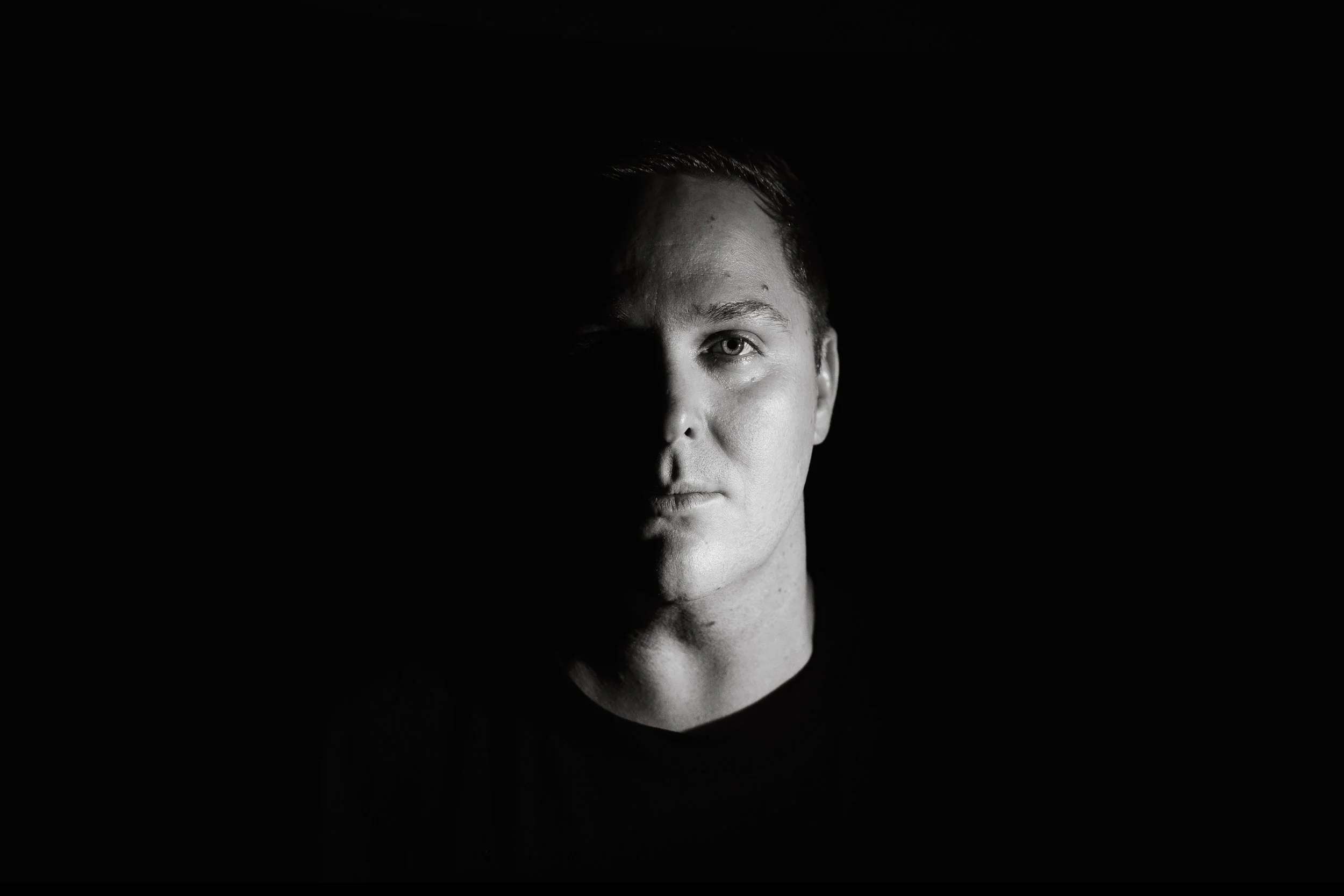 Half of a man's face, shown in black and white, with the other half shrouded in shadow.