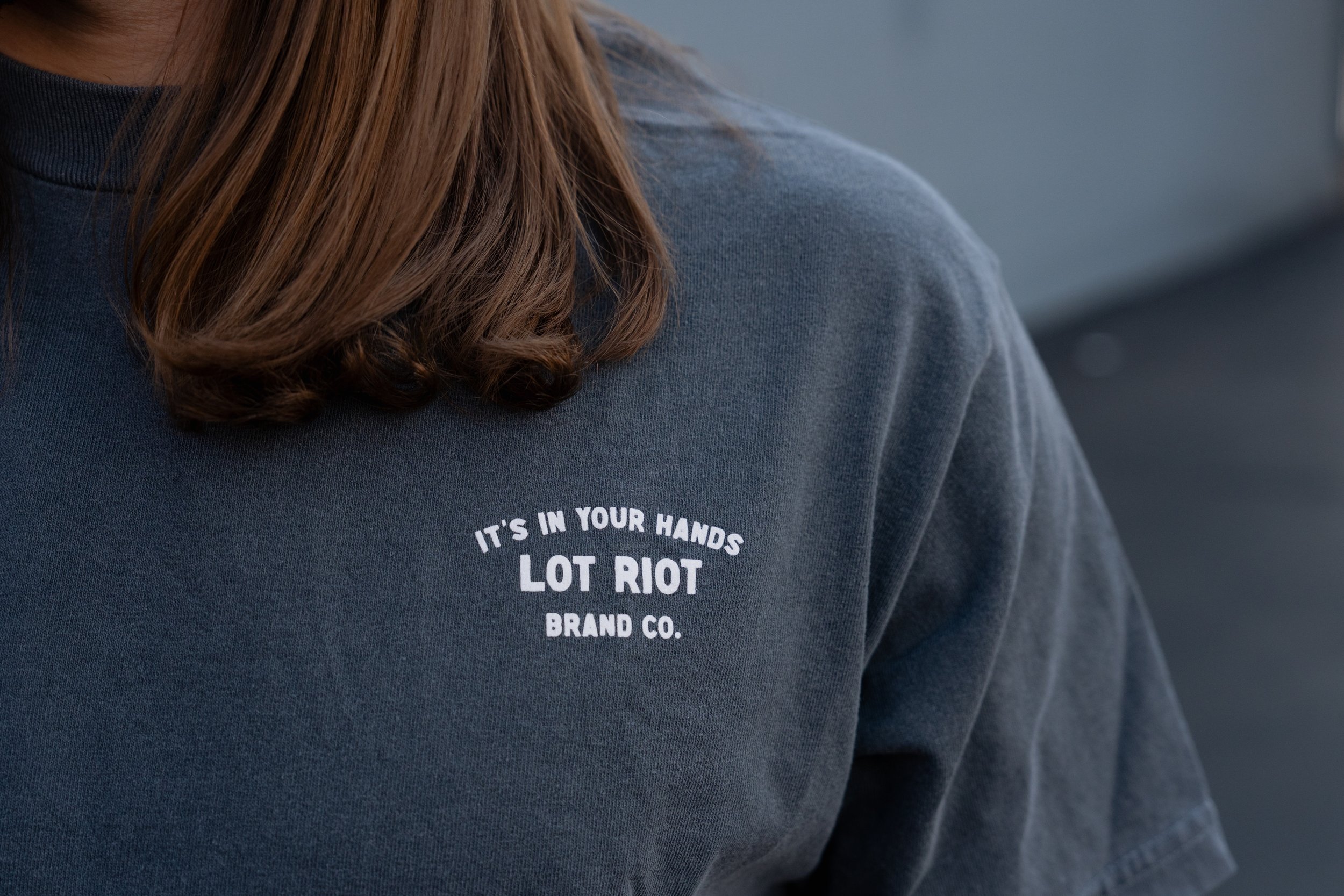 A person wearing a dark gray T-shirt with white text on the front. The person's long, wavy brown hair is visible, and they are at WGI Finals in Dayton, Ohio.
