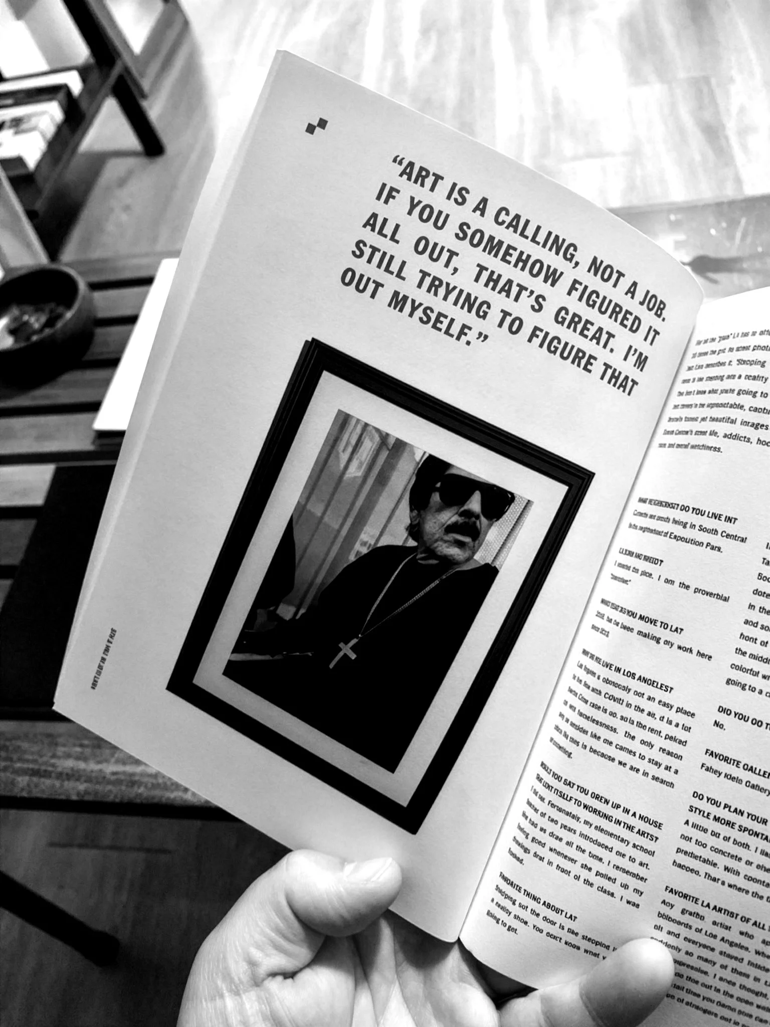 A person holding an open magazine or booklet with a quote on the left page that reads, "Art is a calling, not a job. If you somehow figured it all out, that's great. Still trying to figure that out myself." The right page contains text, likely part o