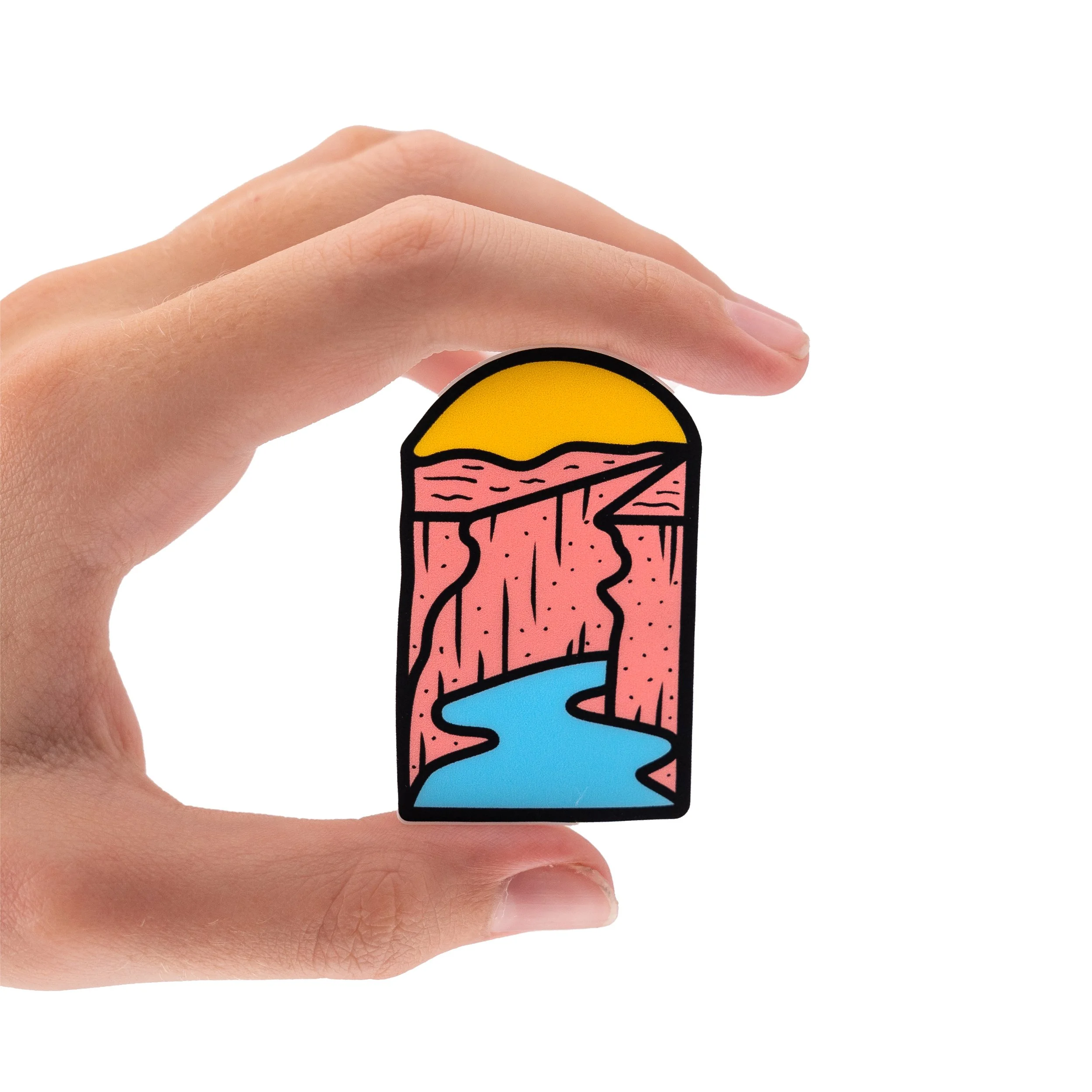 A hand holding a colorful sticker with a graphic of the Colorado River with yellow and blue layers.