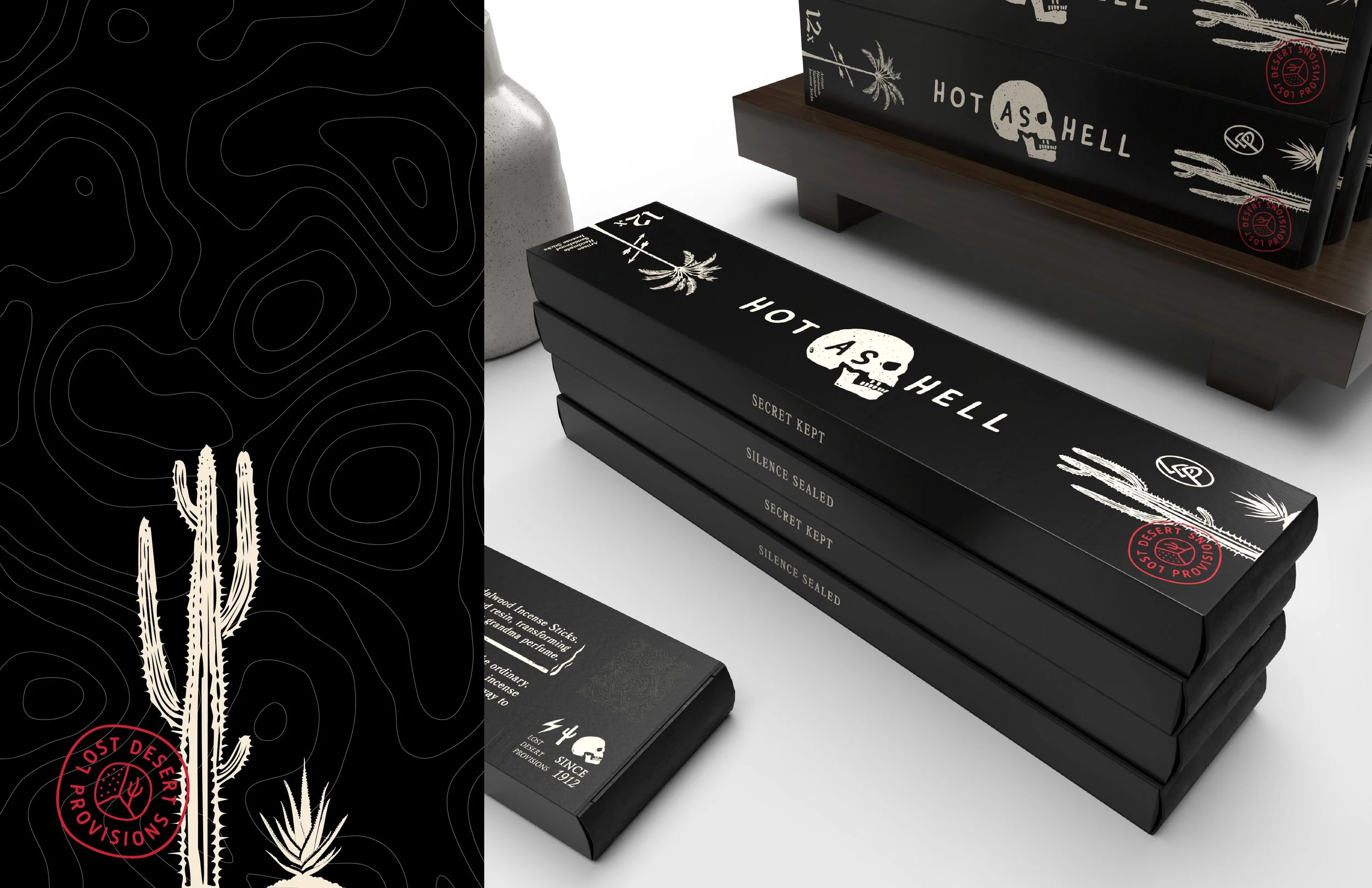 Stack of black boxes and packages with white text and designs, featuring a skull with a palm tree, cacti, and desert imagery, some with red circular stamps reading 'Lost Desert Provisions.' The items are arranged on a white surface with decorative it