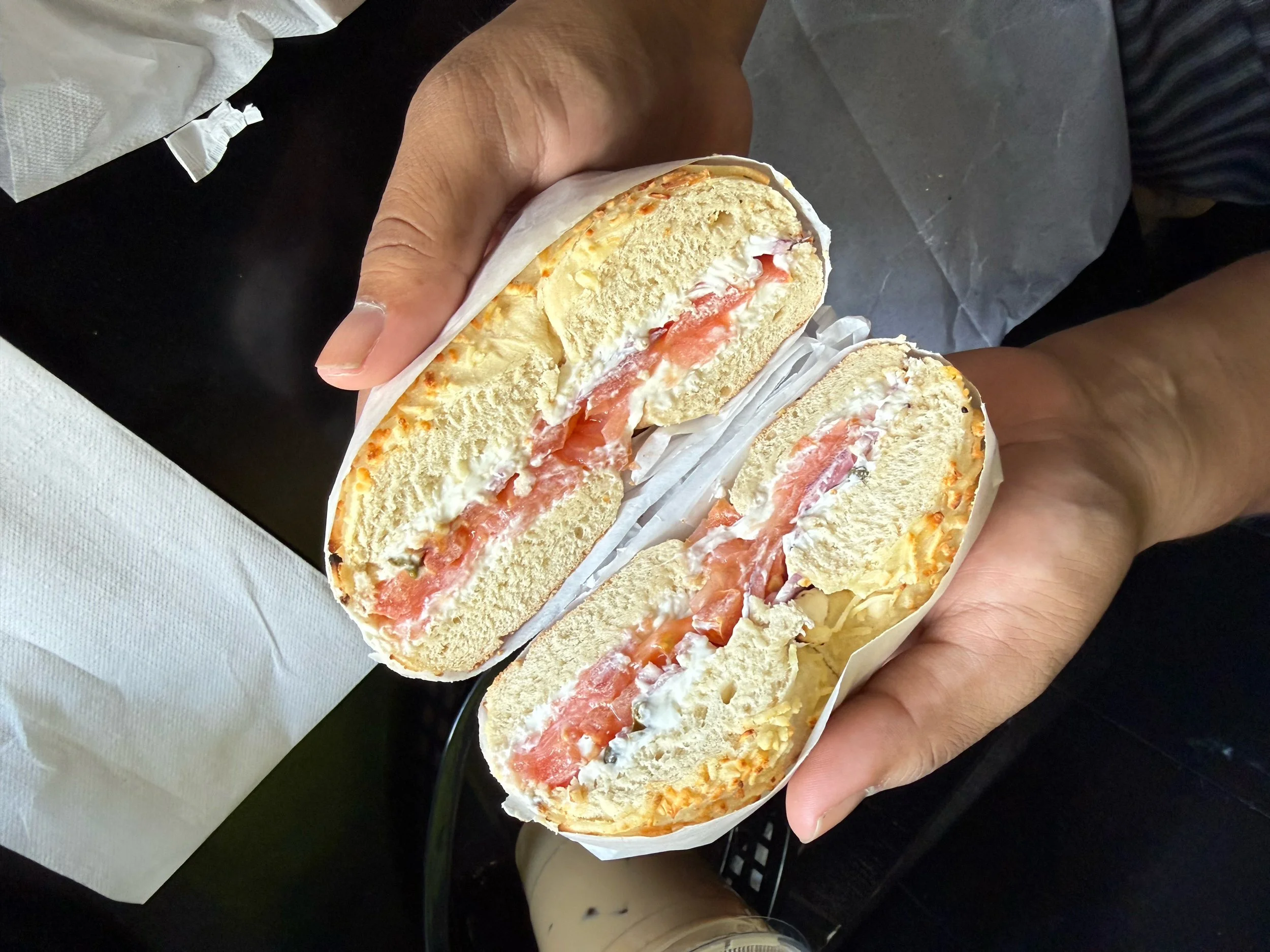 A person holding a sliced sandwich wrap with cream, tomato, and shredded cheese inside.