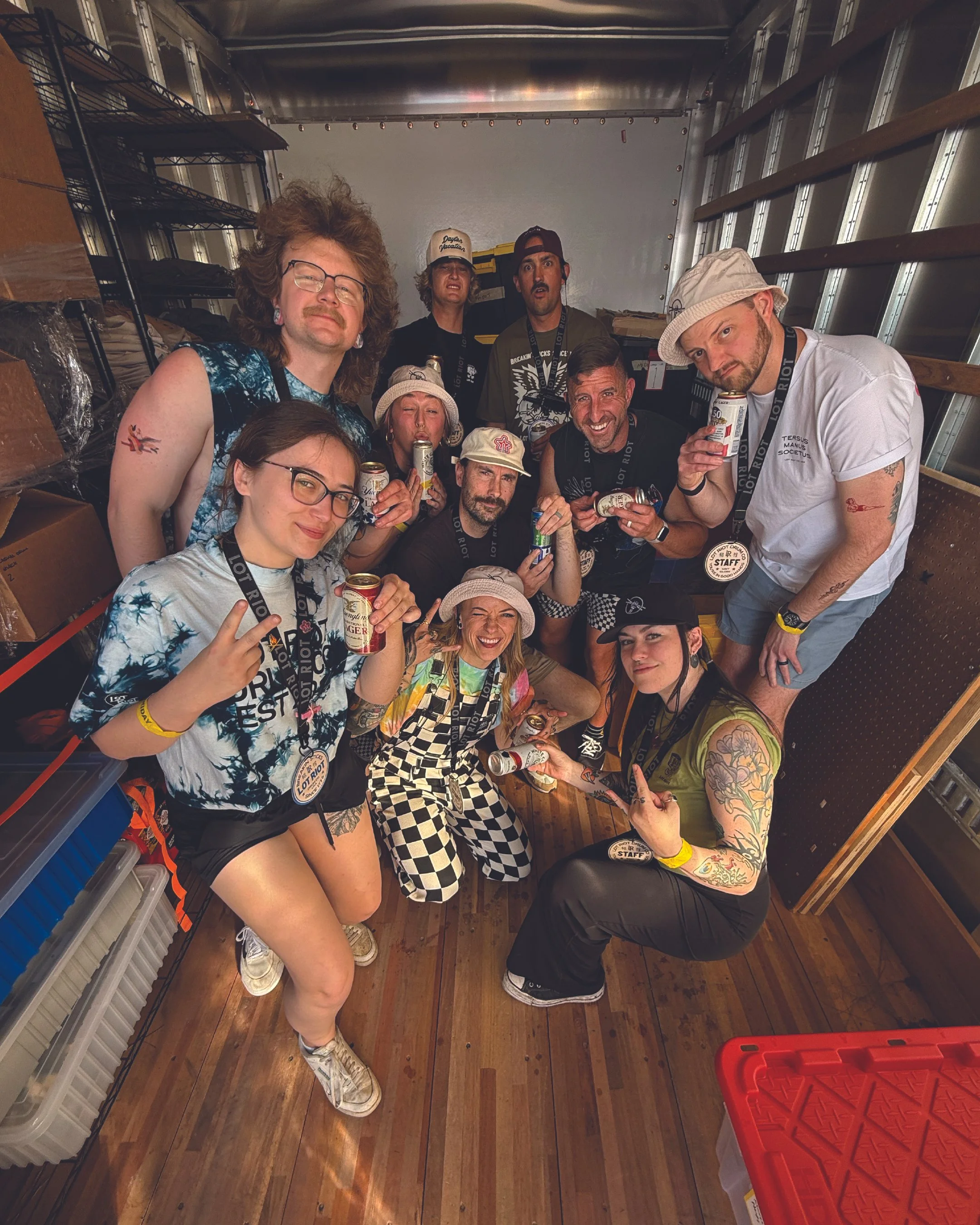 A group of people posing for a photo inside a storage container or truck, holding drinks and making various gestures. They are smiling and appear to be enjoying themselves.