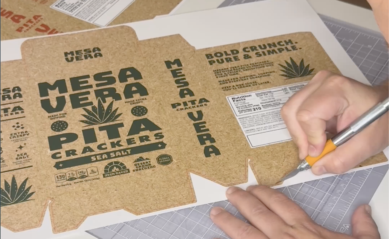 A printed packaging comp being cut by hand on a cutting mat