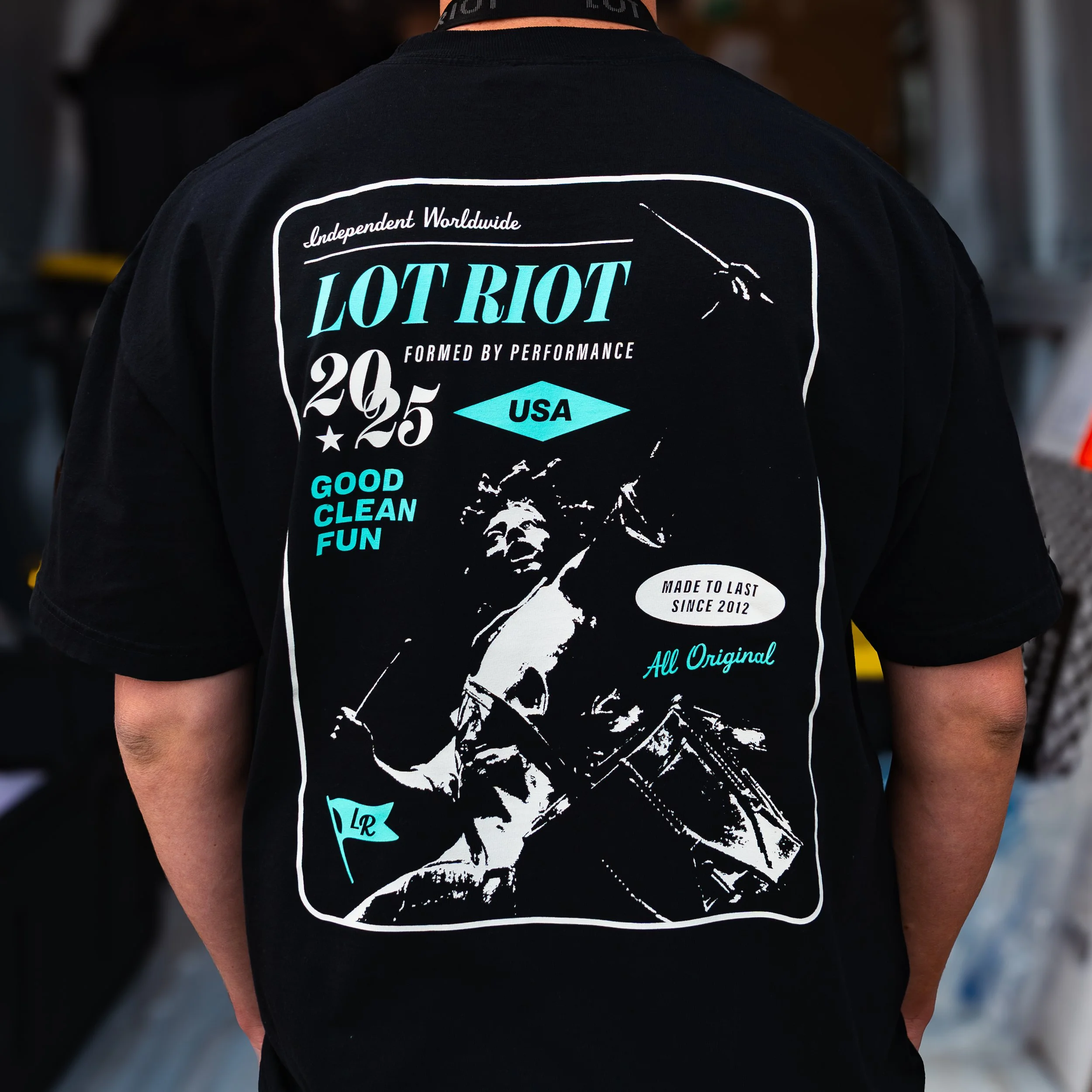 Person wearing a black LOT RIOT t-shirt with graphic and text, back view.