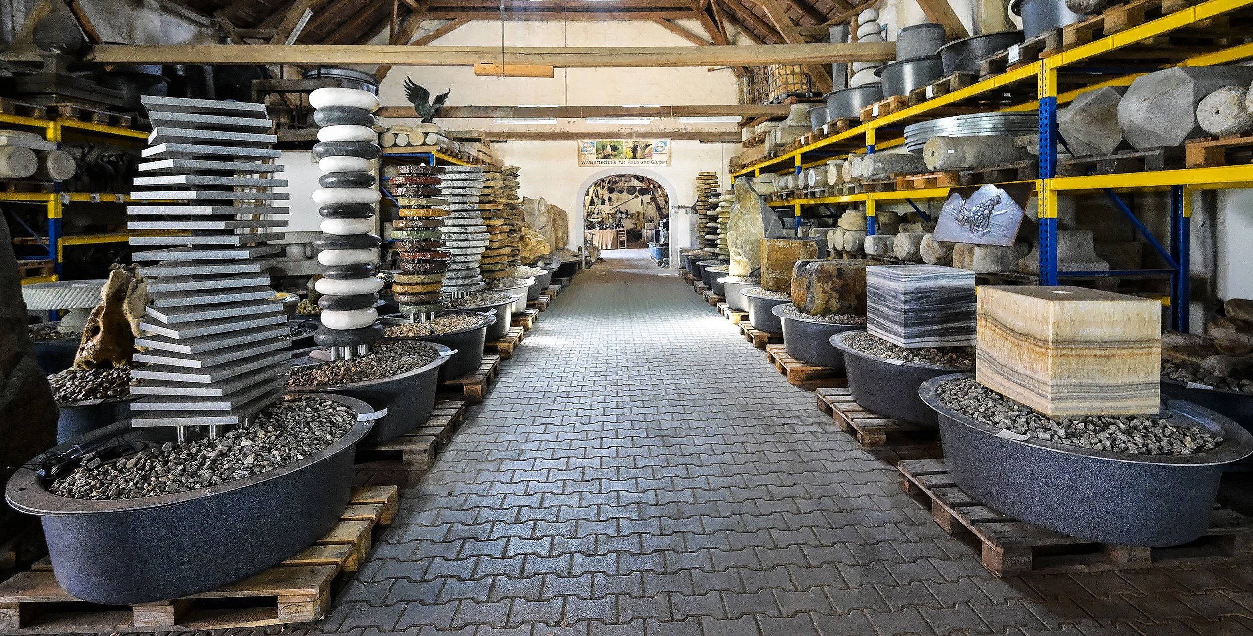 Unternehmensreportage Czernei Natursteinhandel: Schauhalle mit Natursteinbrunnen, Findlingen und weiteren Natursteinelementen.