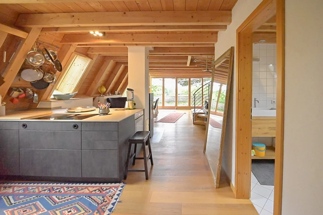Immobilienfotografie Thalham: Offener Wohn- und Küchenbereich im Dachgeschoss mit Holzdecke und Wendeltreppe.