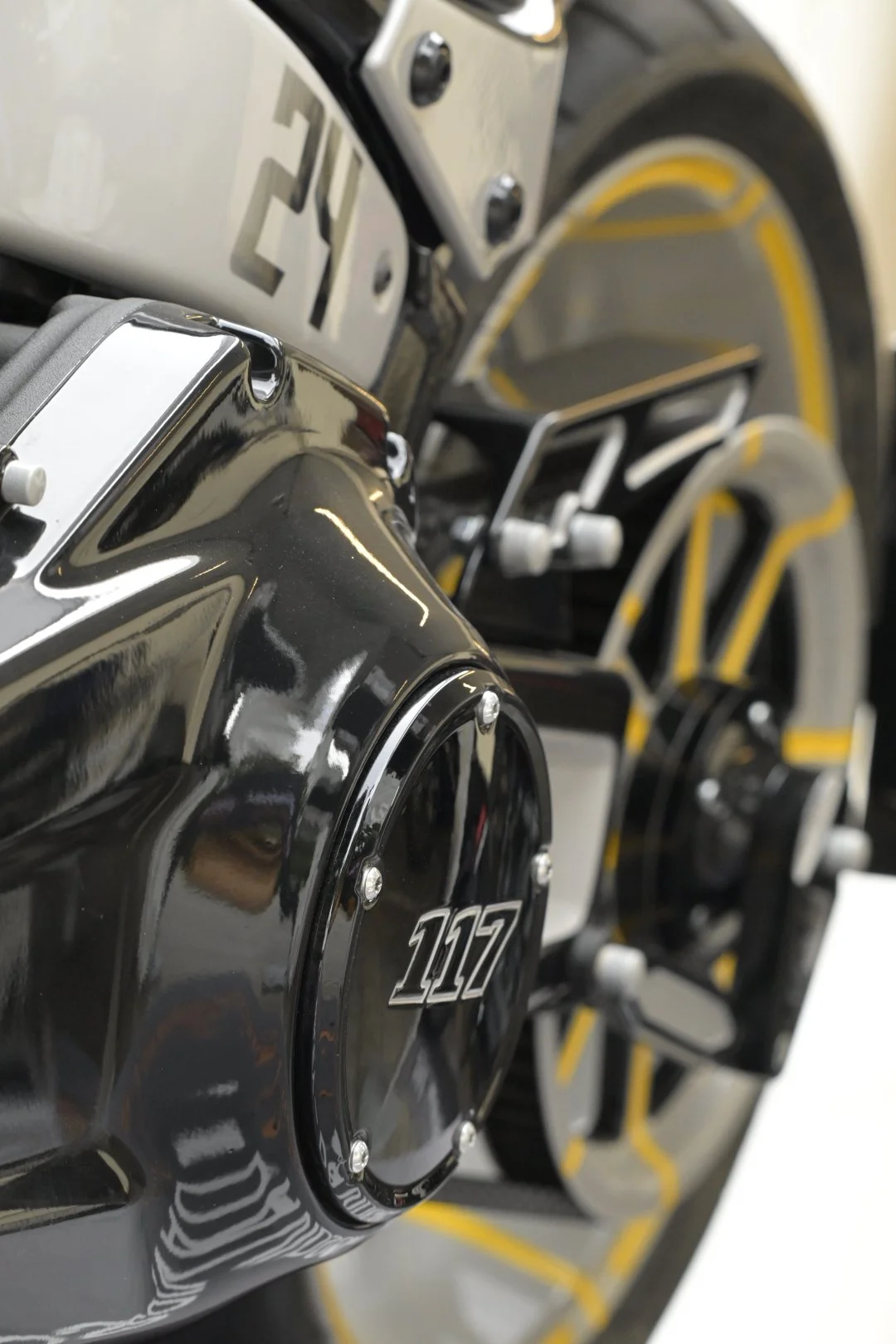 Nahaufnahme eines glänzend schwarzen Motorrads mit „117“-Emblem, verchromten Bauteilen und schwarz-gelben Speichenrädern
