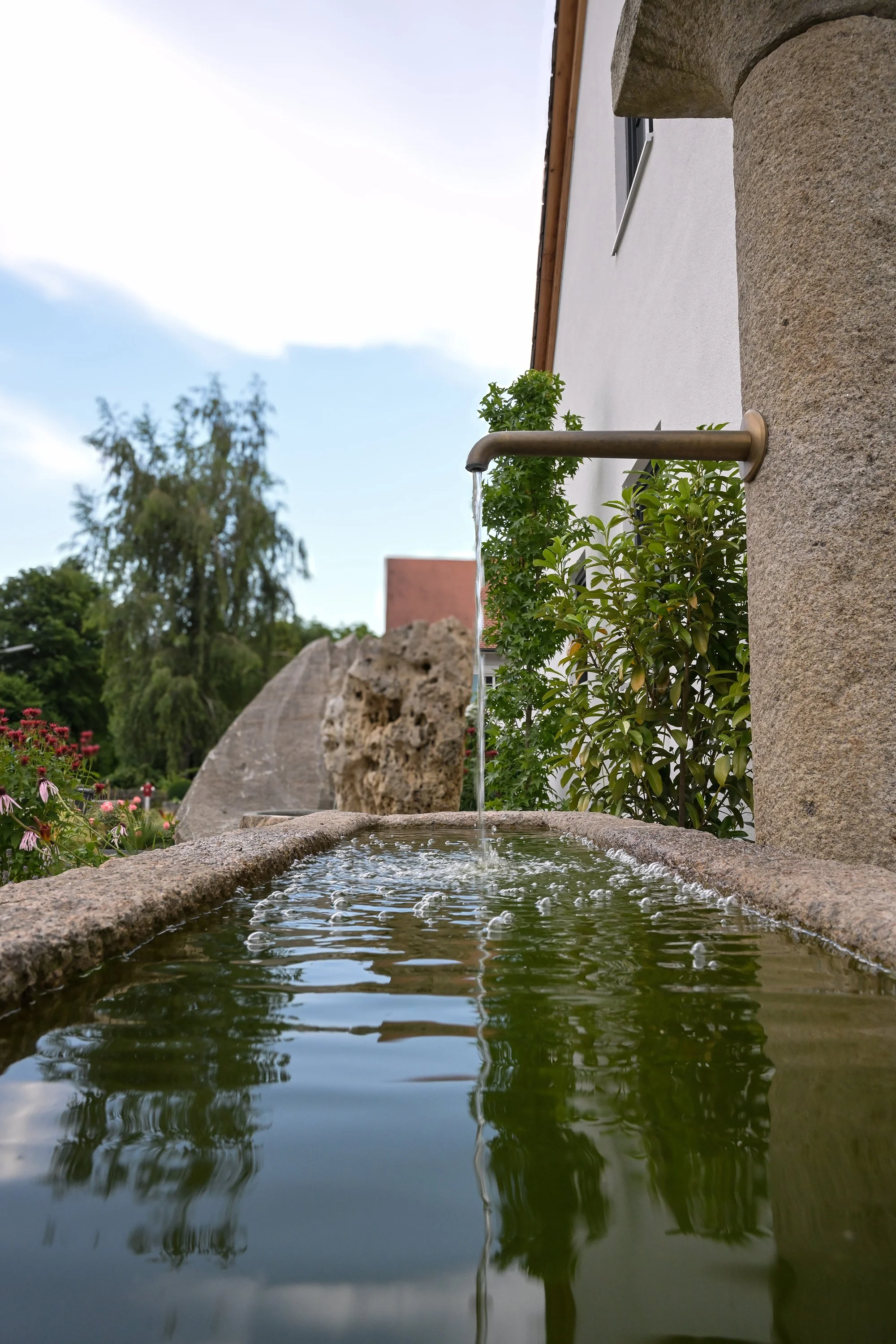 Produktfotografie Czernei Natursteinhandel: Natursteinbrunnen mit fließendem Wasser im Garten.