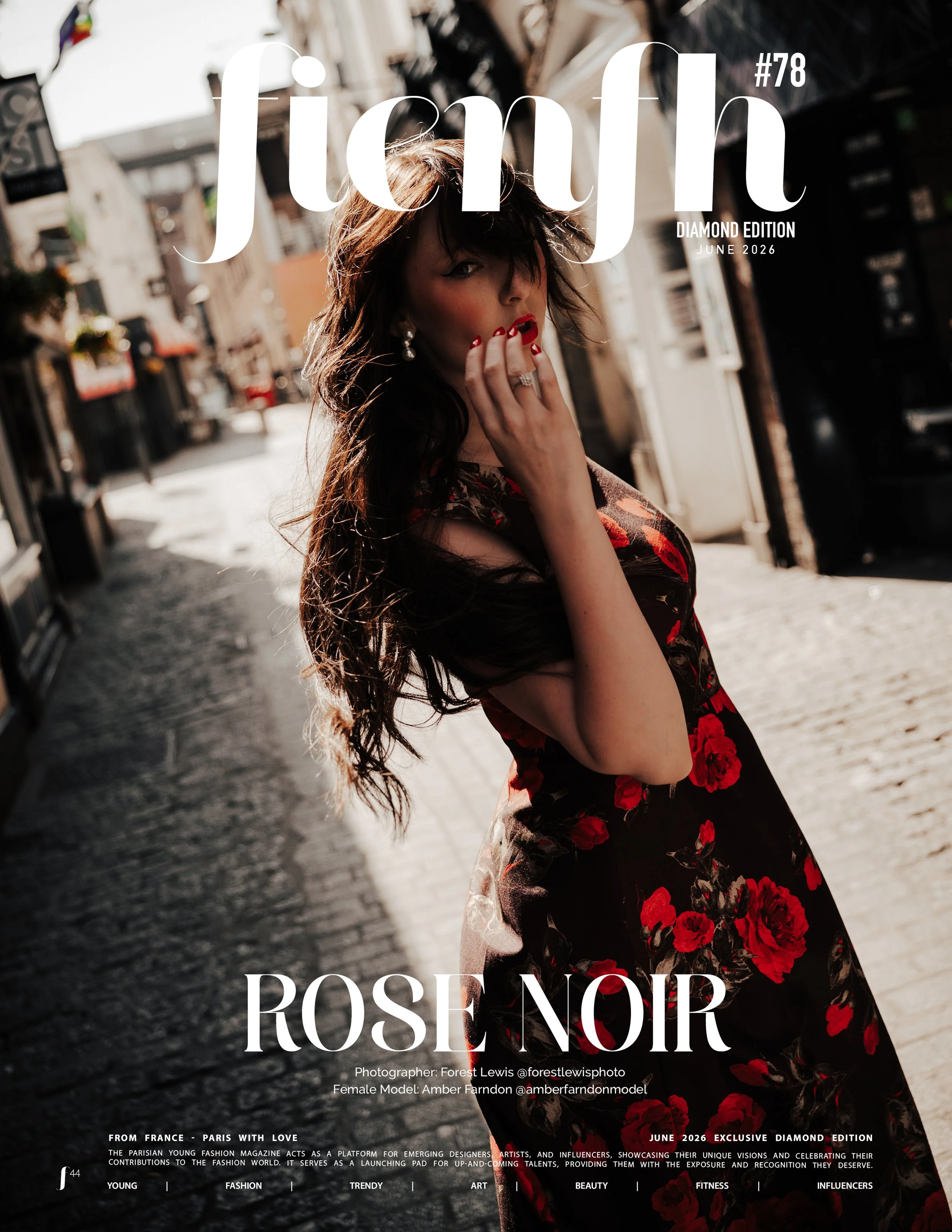This is a magazine cover titled 'fignf #78 Diamond Edition June 2026'. The cover features a female model with dark hair, red lipstick, and red nail polish, wearing a black dress with red floral patterns. The background shows an urban street scene with buildings and cobblestone pavement, bathed in sunlight.
