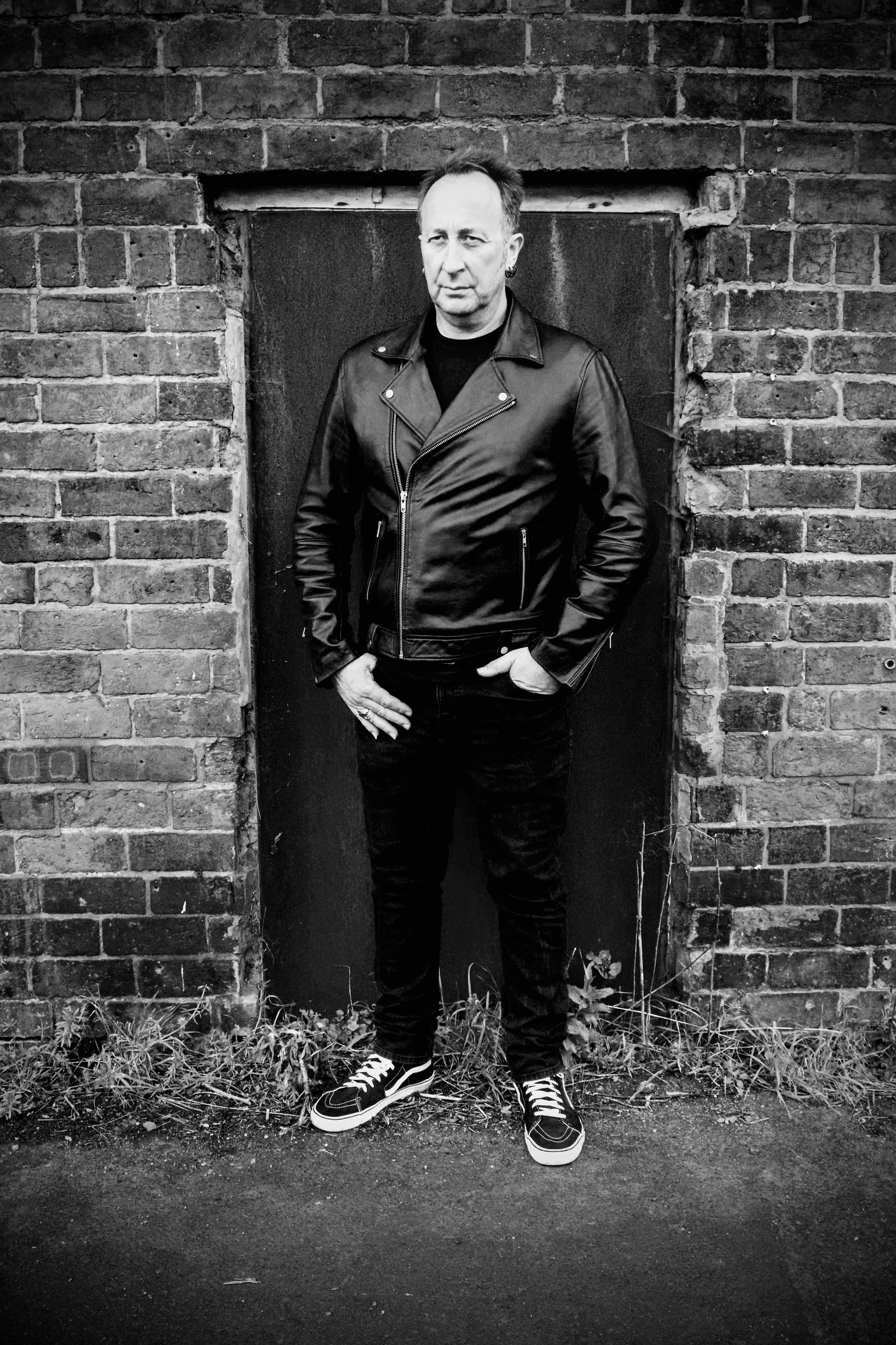 Black‑and‑white portrait of a man in a leather jacket standing against a brick wall — minimalist composition with urban grit and quiet confidence.