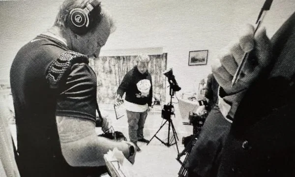 People working on a video or photo shoot in a room, with cameras and equipment set up.
