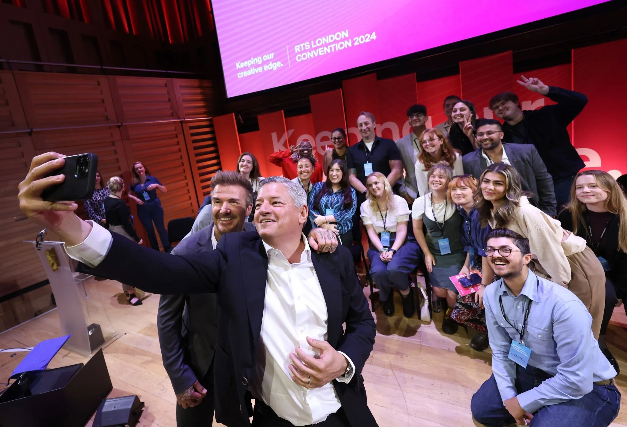 Attendees capturing a lively selfie at a London convention, framed by a glowing screen and the energy of a creative industry event.