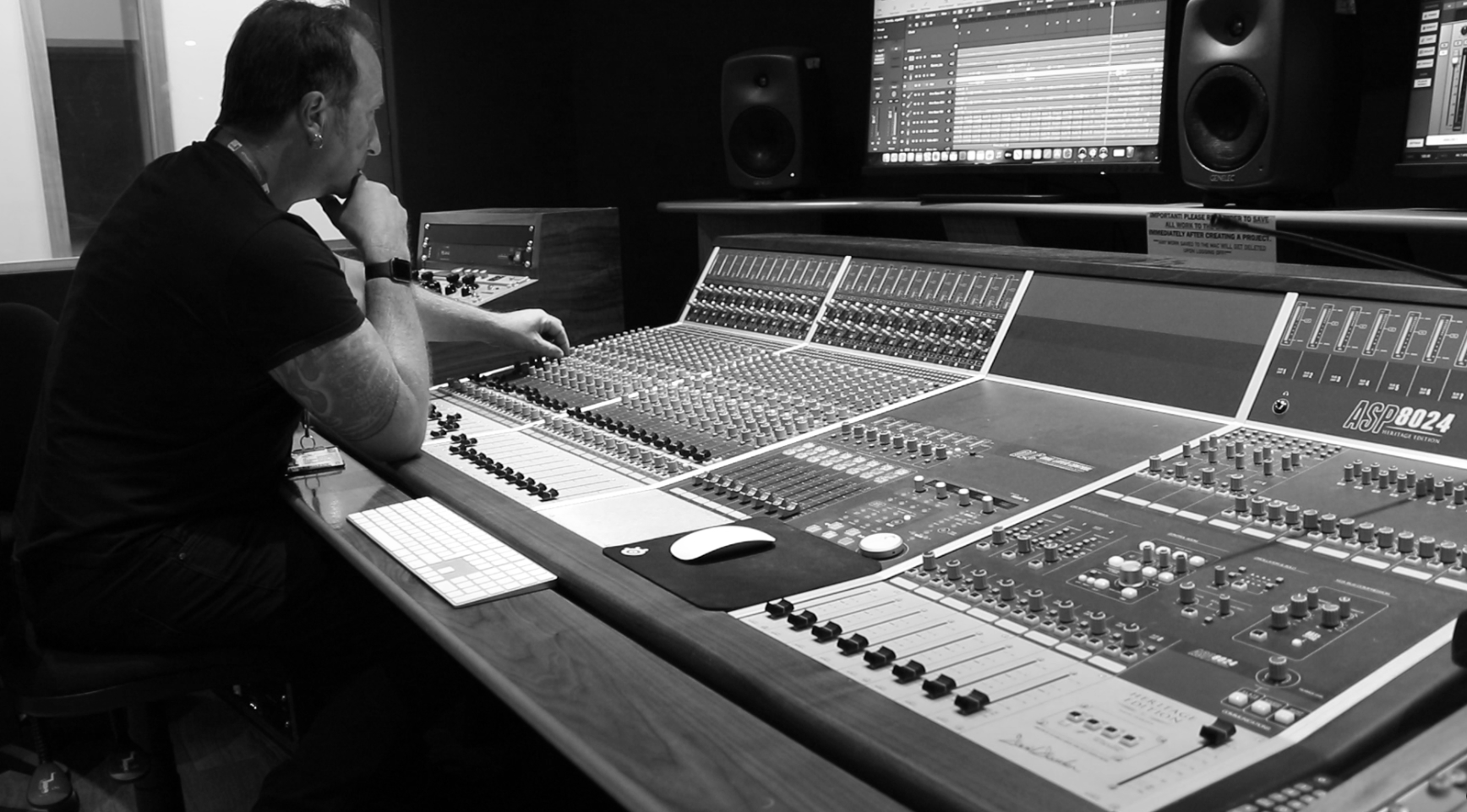 Sound engineer at a mixing console surrounded by monitors and speakers — a focused moment of audio craftsmanship in the studio.