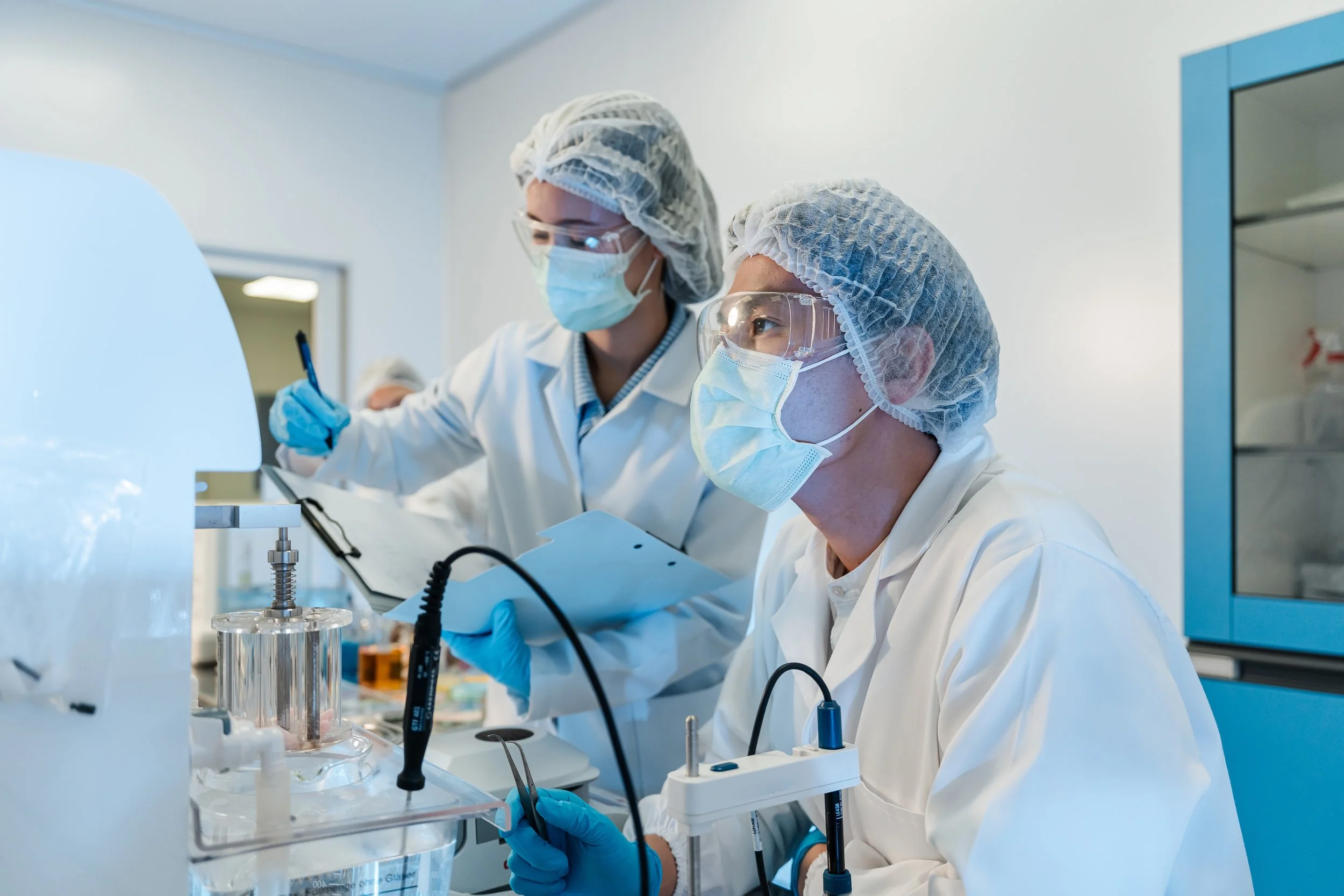 Scientists working in a laboratory wearing protective gear, including gloves, masks, hair covers, and safety goggles, as they conduct experiments with laboratory equipment.