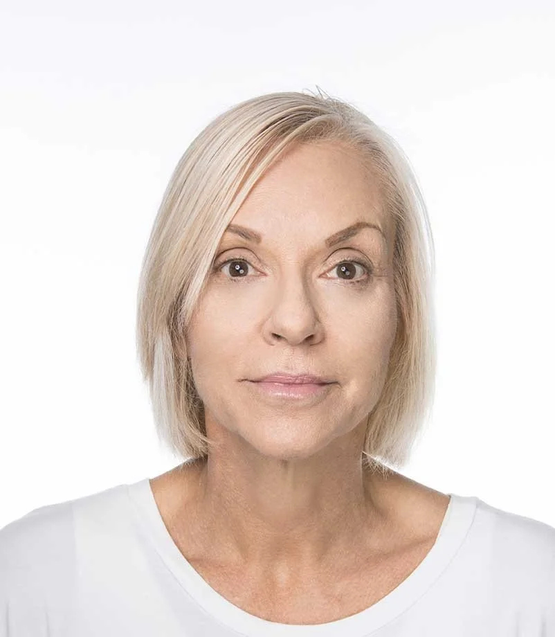 A middle-aged woman with blonde hair and light skin, wearing a white shirt, looking at the camera against a white background.