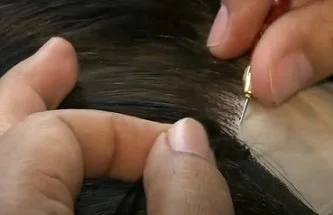 Close-up of a person getting a hair extension or strand inserted by a technician.