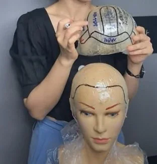 Person holding a mannequin head and drawing on a round object that resembles a brain with markers.