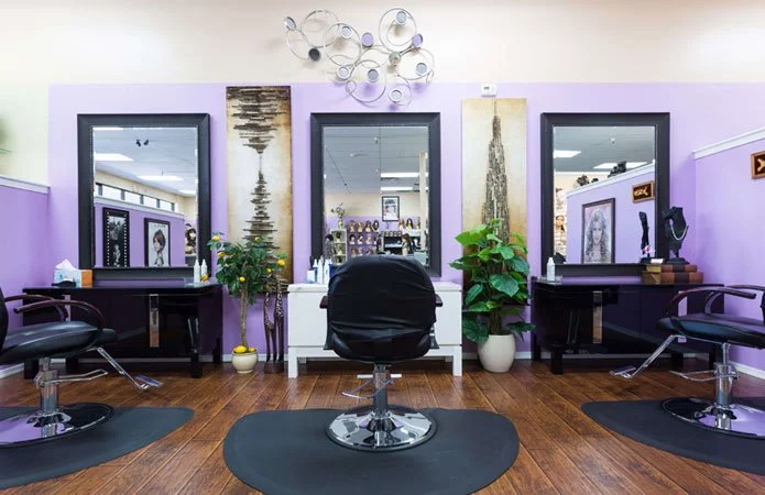 Beauty salon with three styling stations, mirrors, chairs, and decorative wall art, featuring purple walls and wooden floors.