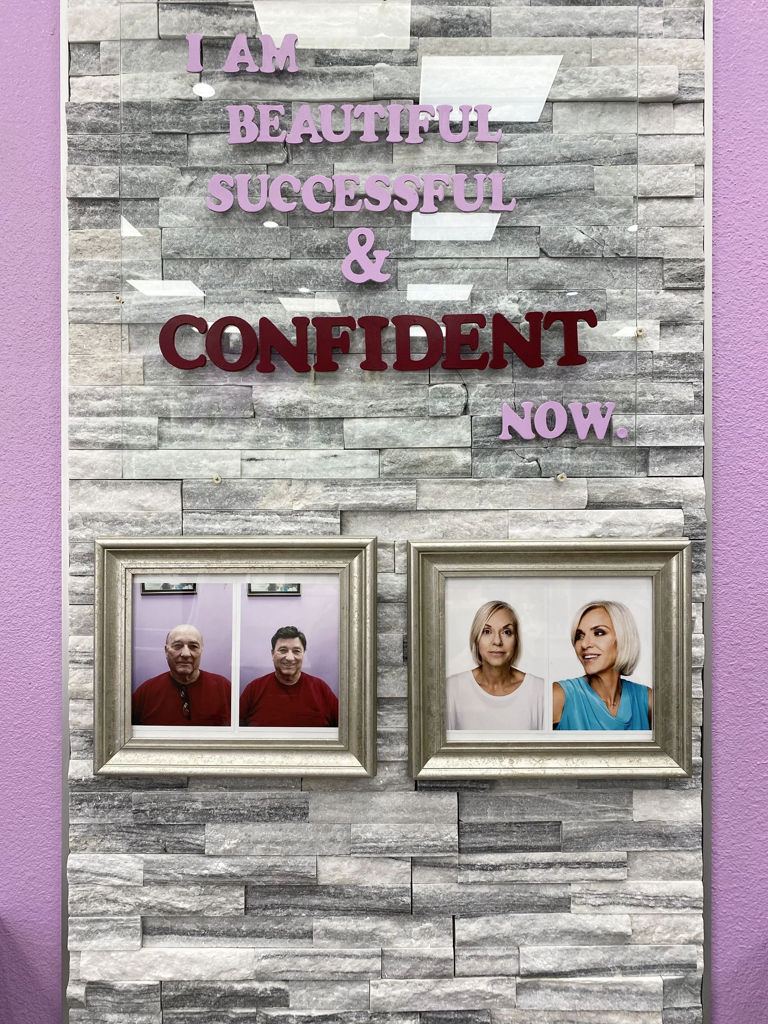 Decorative wall with the words "I am beautiful, successful, confident, now" in purple and red letters, and framed photographs of two elderly men and two elderly women below the words.
