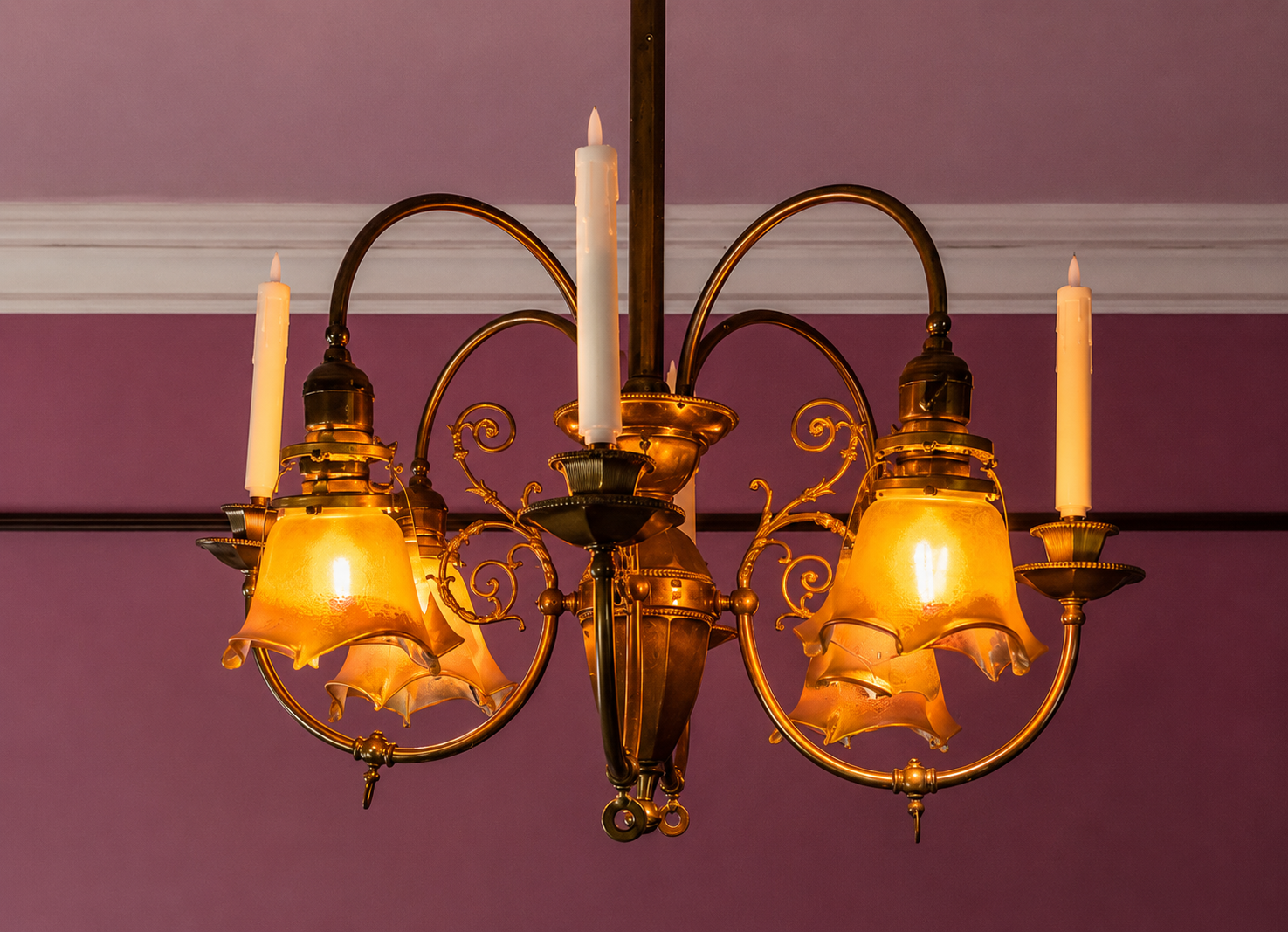 A vintage brass chandelier with five amber-colored glass lampshades, mounted on a purple wall ceiling.