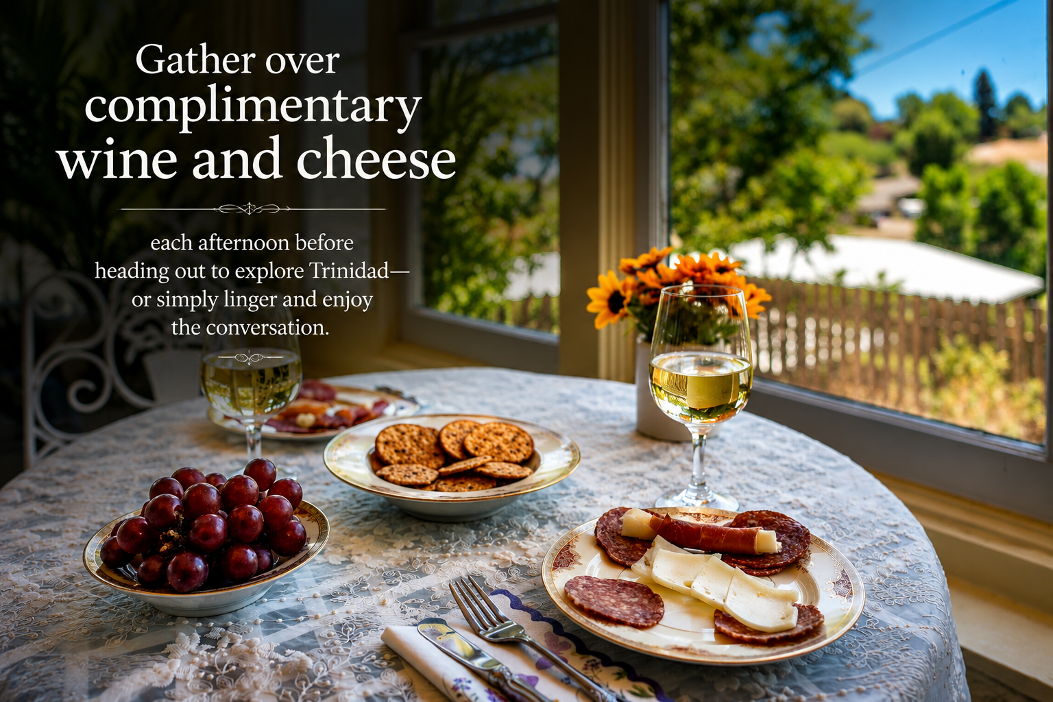 A table with wine glasses, cheese, cured meats, grapes, and cookies, set by a window with green trees outside, promoting a wine and cheese gathering.