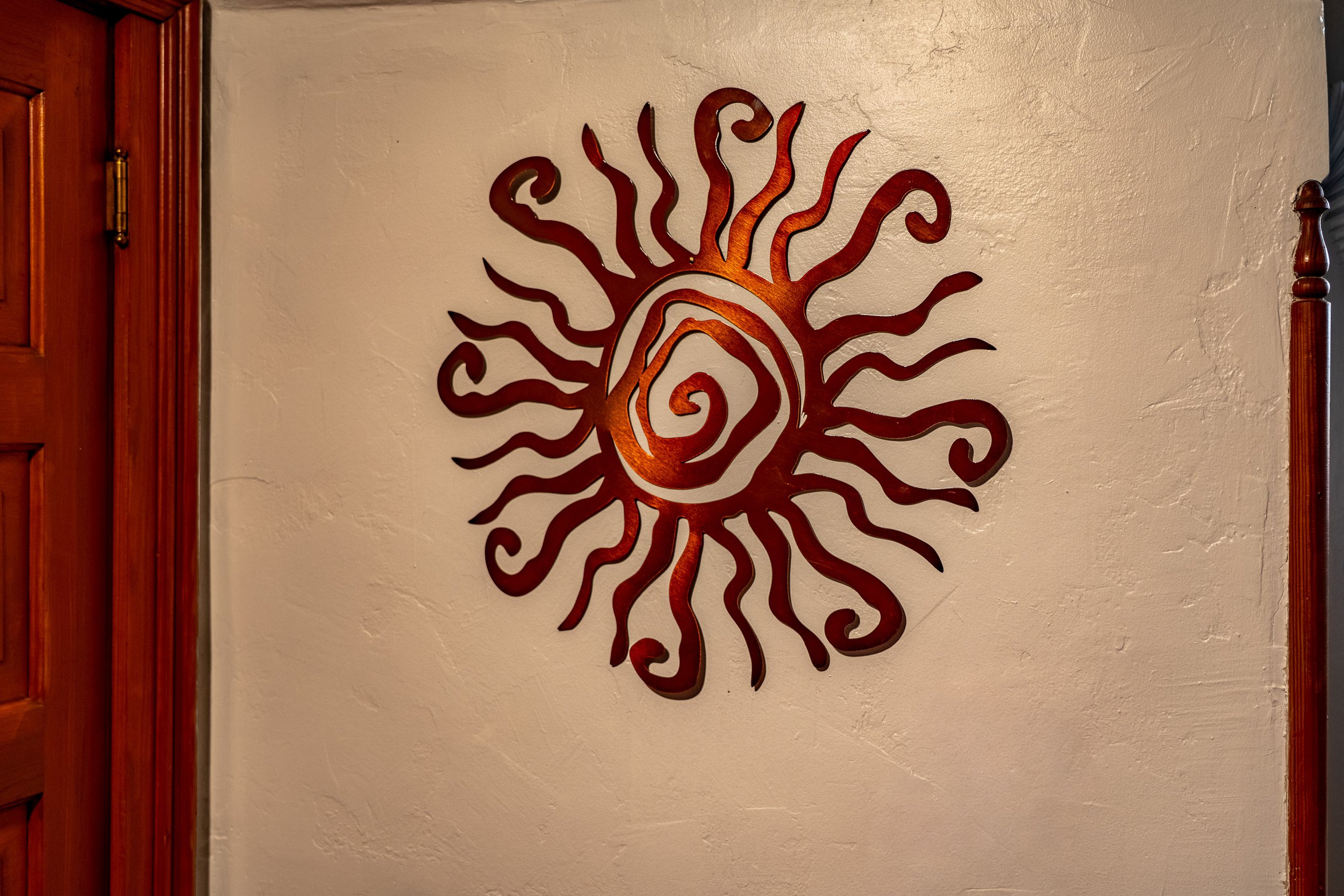 Decorative wall art resembling a stylized sun with swirling rays, mounted on a beige textured wall between wooden door frames.