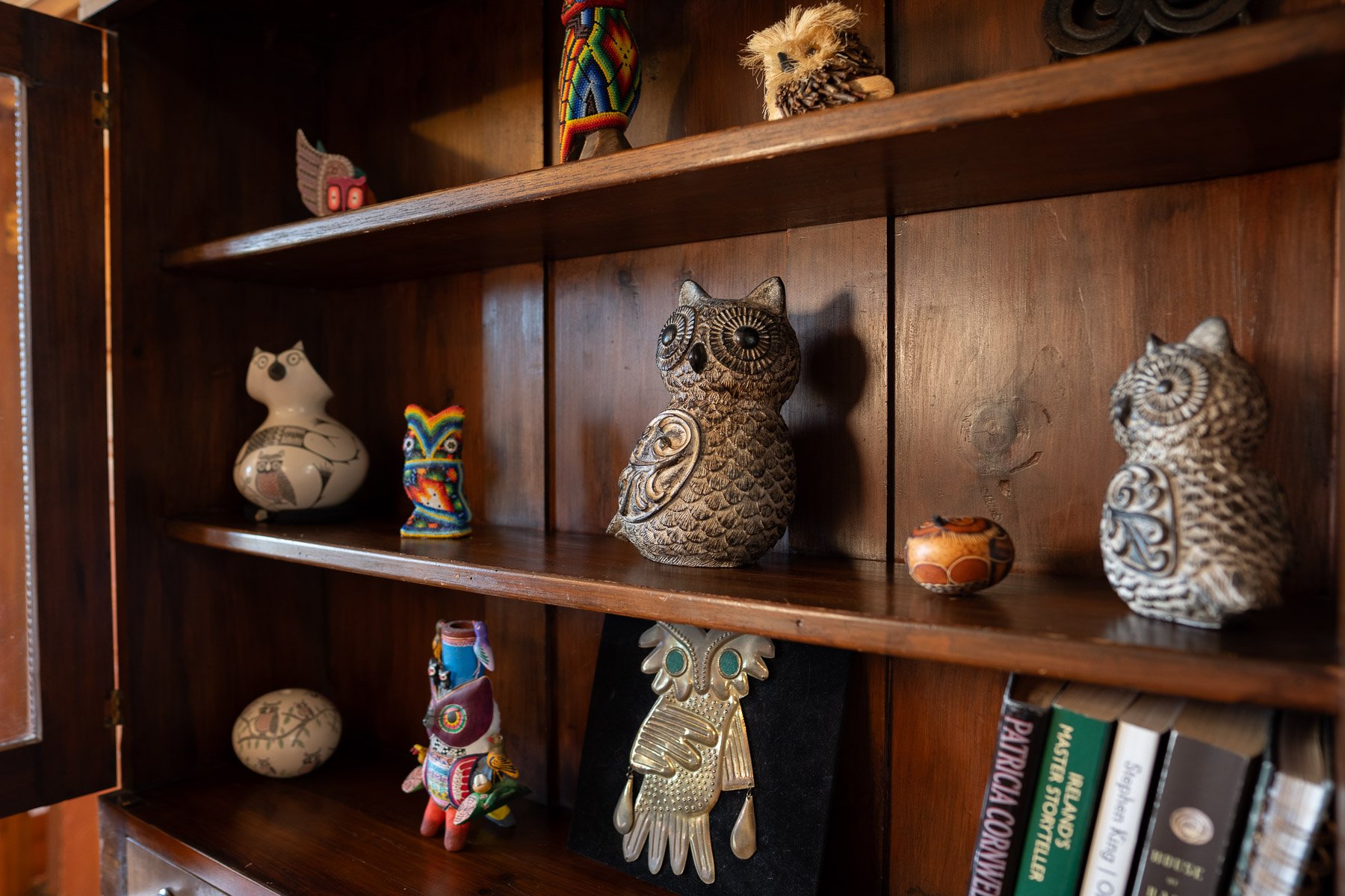 Wooden bookshelf with decorative owl figurines and small colorful animal figurines on the shelves.