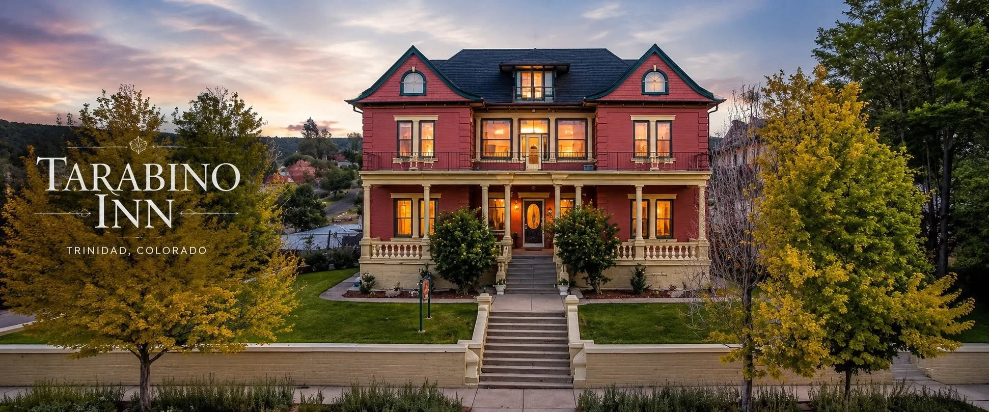 A large, Victorian-style house with a red exterior, multiple windows, and a front porch overlooking stairs, set against a sunset sky, surrounded by trees with green and yellow leaves. The text overlay reads "Tarabino Inn, Trinidad, Colorado."