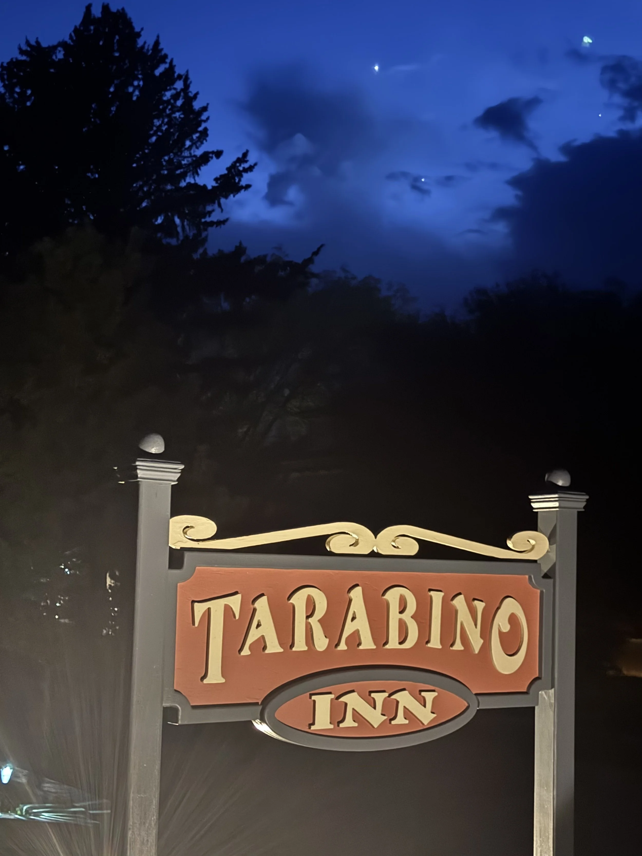 Sign for Tapario Inn with decorative metalwork, located outdoors at night, illuminated by exterior lights, with trees and cloudy night sky in the background.
